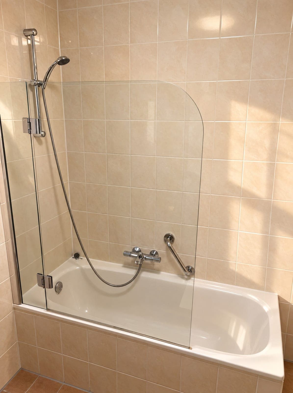 Badkamer met ligbad, douche met glazen scherm en een handgreep